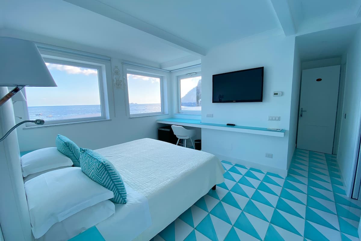 A room with a bed, a desk, a TV, and a view of the sea.