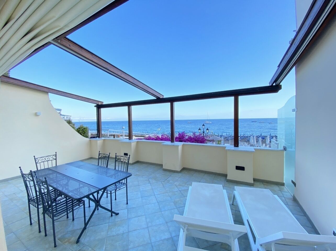 Una terraza en la azotea con mesa y sillas, vista al mar y cielo despejado.