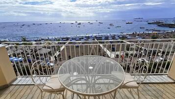 A balcony with a round table and chairs, overlooking a beach with numerous boats and umbrellas.