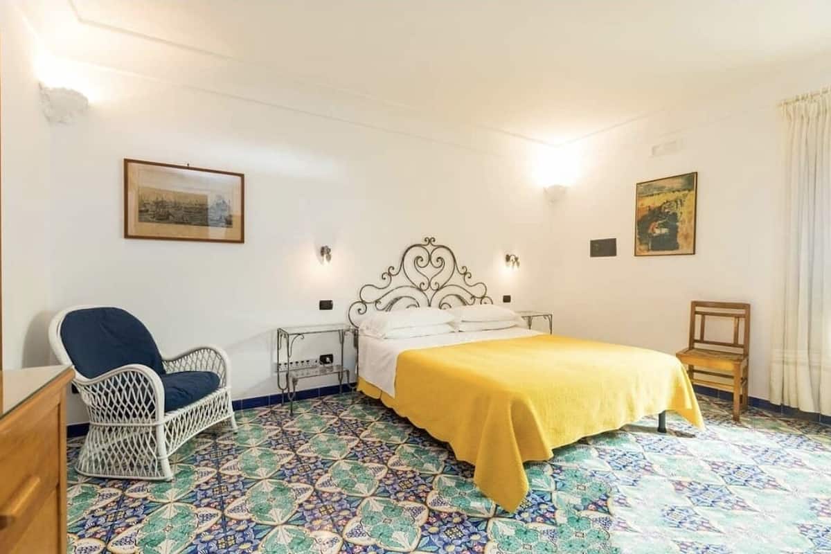 A room with a bed, a chair, a nightstand, and a wall with two framed pictures.