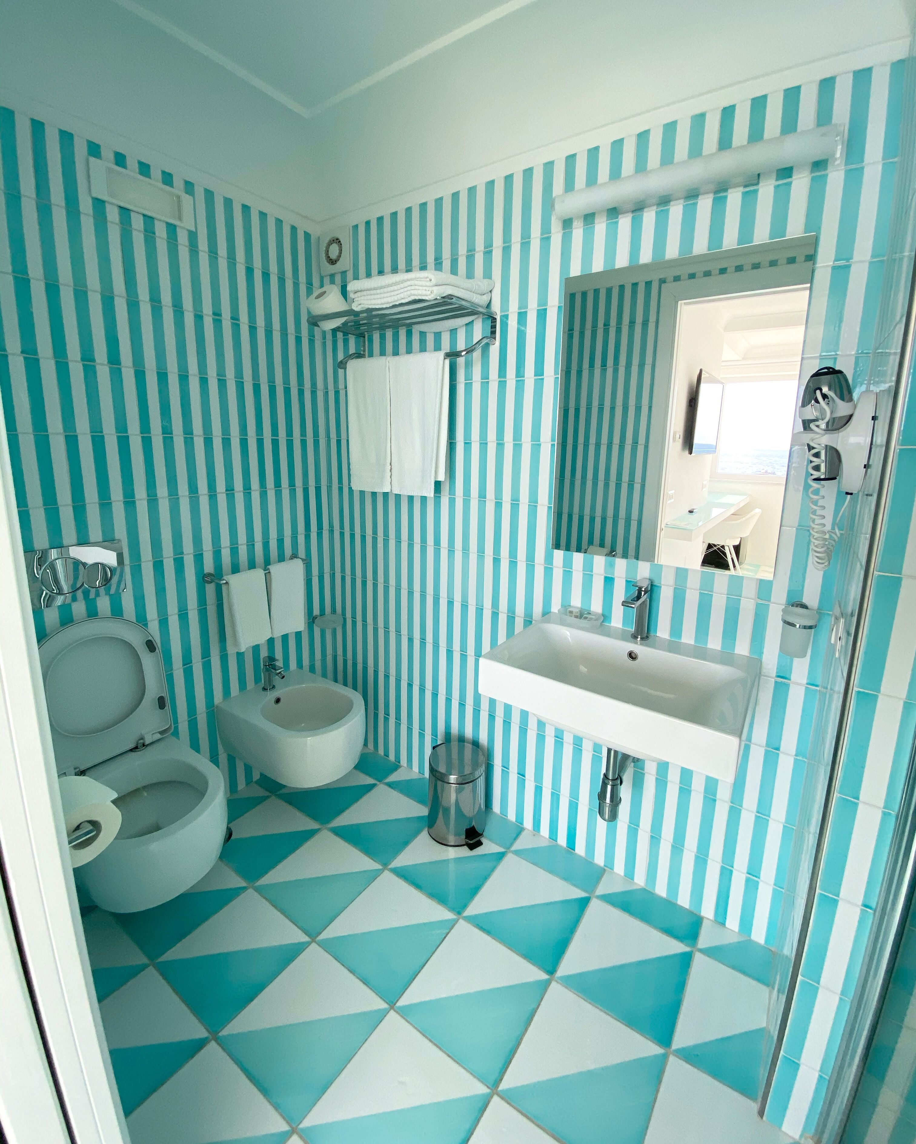 A bathroom with a striped tile wall, a sink, a toilet, and a bidet.