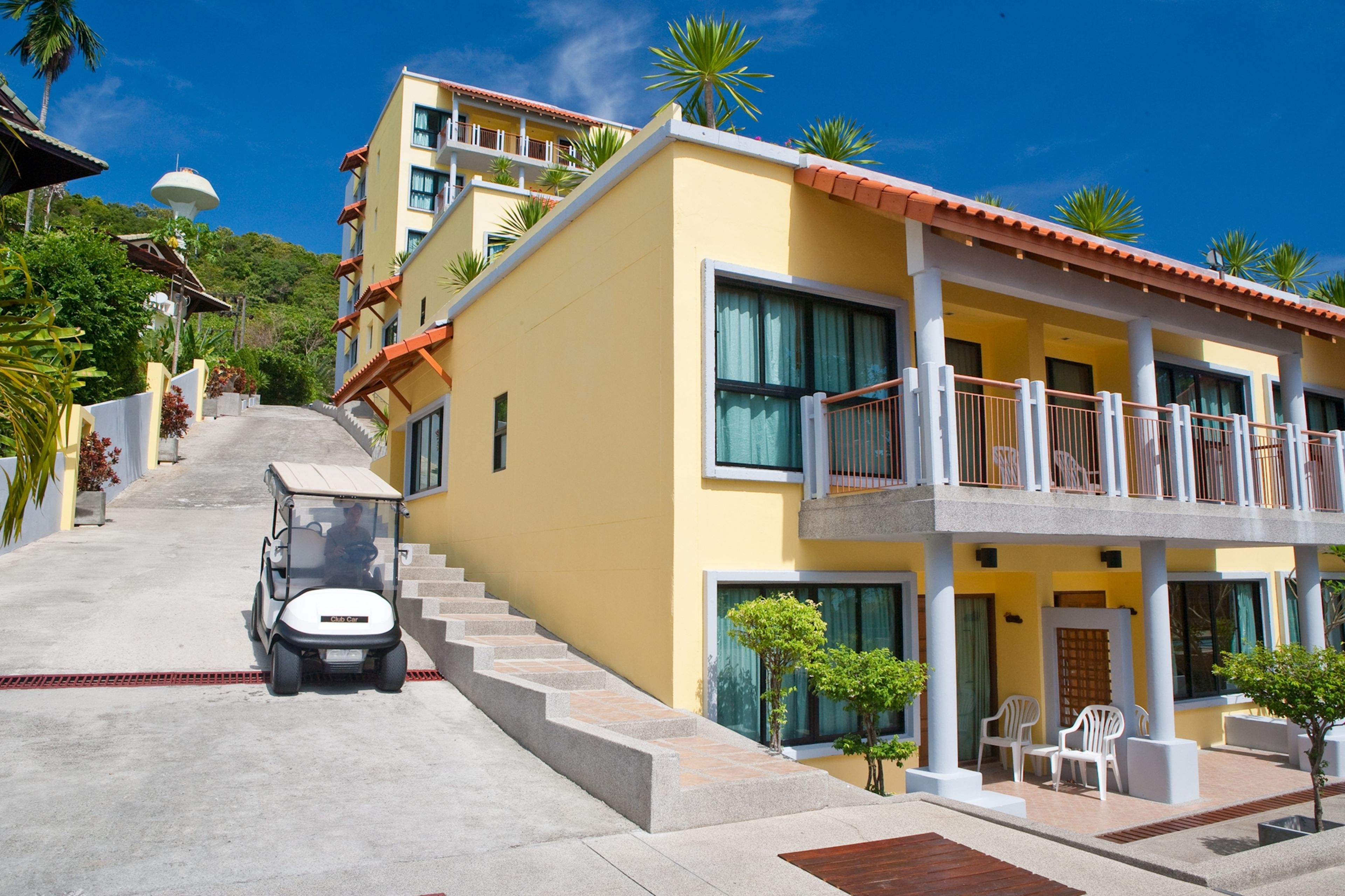 A yellow building with a red roof, a balcony, and a small vehicle parked in front.