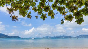Une plage bordée d’une eau turquoise et limpide, avec des bateaux et des montagnes qui se dessinent à l’horizon.