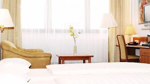 A hotel room with a bed, a desk, a chair, a lamp, a vase with flowers, and a television. - Fair Hotel am Rathaus (Schwalbach am Taunus)