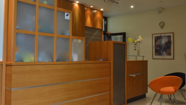 A reception area with a wooden reception desk, a glass partition, and a clock on the wall. - Fair Hotel am Rathaus (Schwalbach am Taunus)