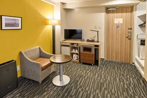 A hotel room with a single sofa, a small round table, a television, a minibar, and a wooden door. - Smile Hotel Tokyo Asagaya (Tokyo)
