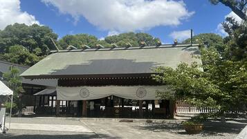 A traditional building with a tiled roof, a covered entrance, and a garden area with a tree and a bench.