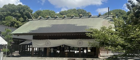 A traditional building with a tiled roof, a covered entrance, and a garden area with a tree and a bench.