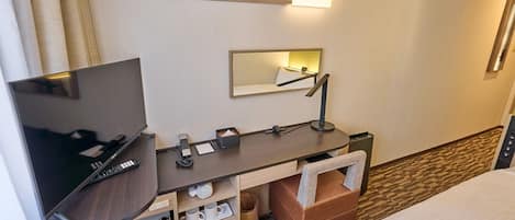 A hotel room with a bed, a desk with a TV, a mirror, and a small kitchenette area.