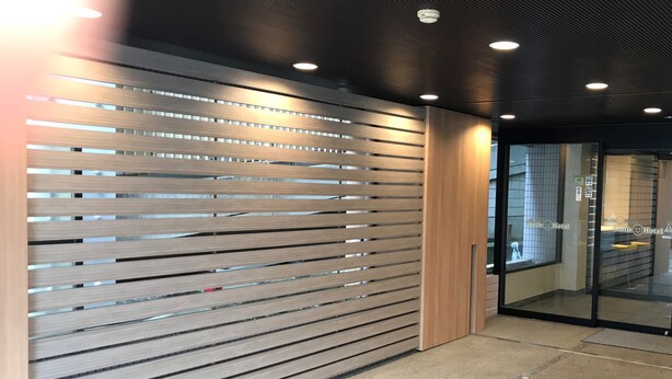 A modern interior with a slatted wall design, recessed ceiling lights, and a glass door leading to a room. - Smile Hotel Tokyo Asagaya (Tokyo)