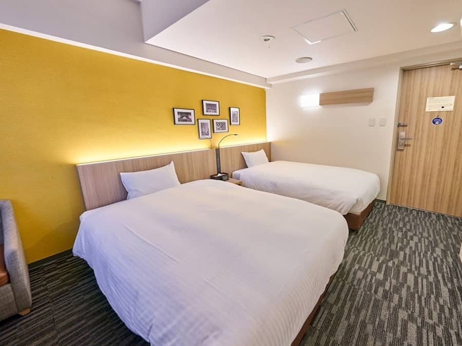 A hotel room with two beds, a chair, and a door with a sign.