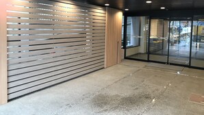 A modern hotel lobby with a slatted wooden wall, glass doors leading to the reception area, and a ceiling with recessed lighting. - Smile Hotel Tokyo Asagaya (Tokyo)