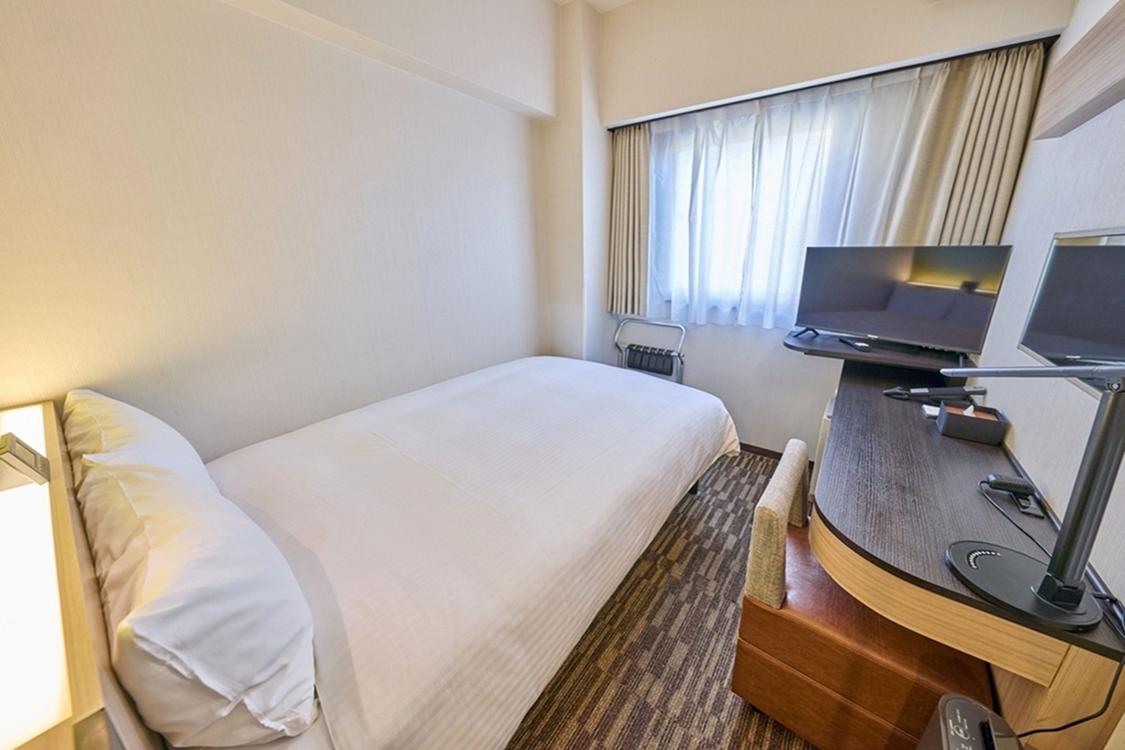 Een hotelkamer met een bed, een bureau met een computer, een televisie en een raam met gordijnen.