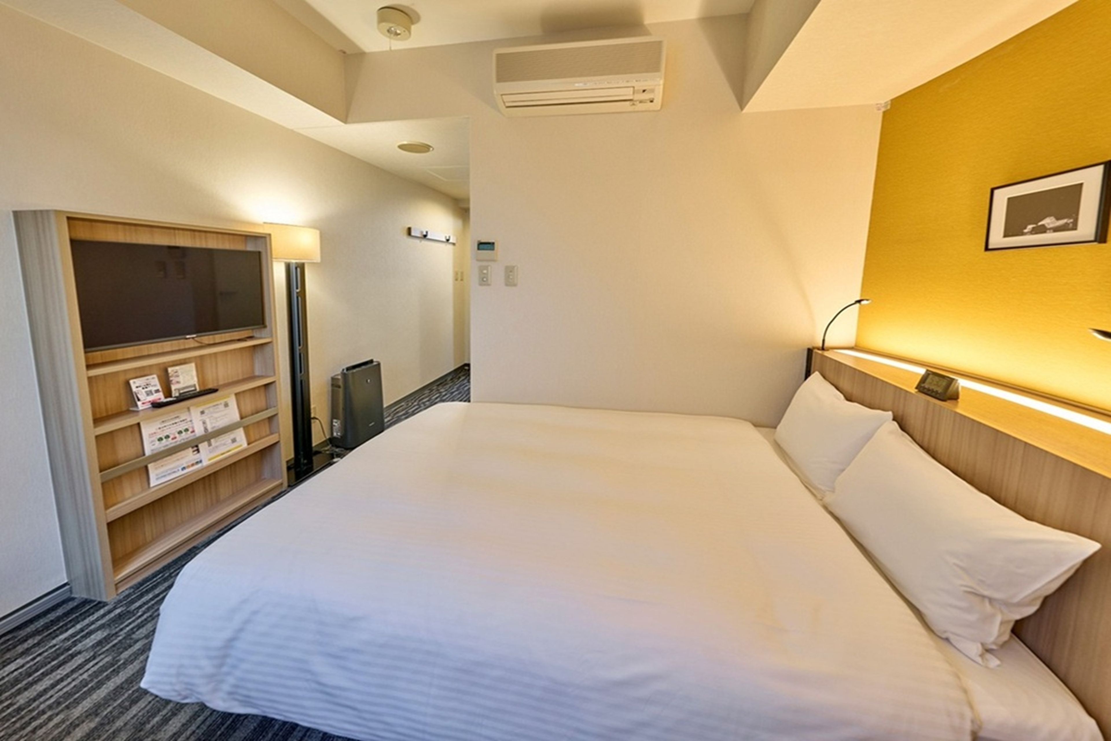 Habitación de hotel con cama, armario, escritorio y aire acondicionado de pared.