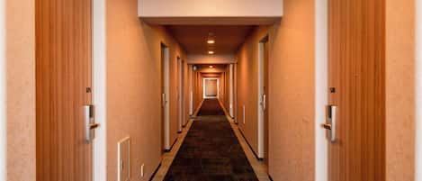 Pasillo de hotel con puertas a ambos lados, piso alfombrado e iluminación en el techo.