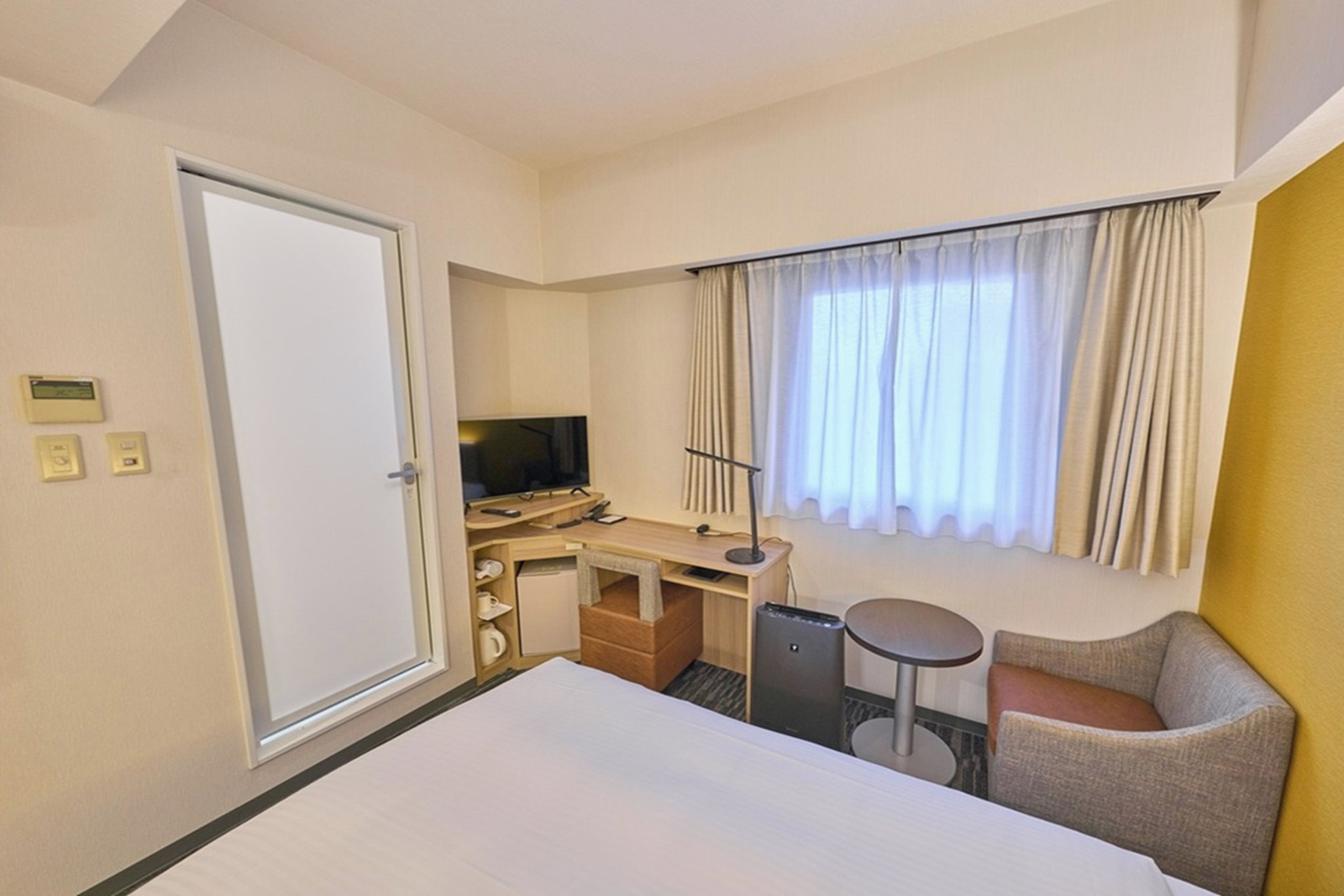Hotellihuone, jossa on sänky, työpöytä, tuoli, televisio ja ikkuna, jossa on verhot.