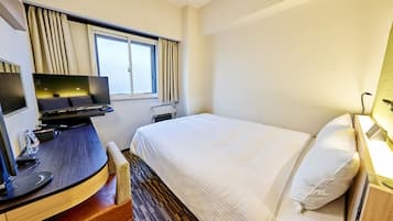 A hotel room with a bed, a desk with a computer, a chair, and a television.