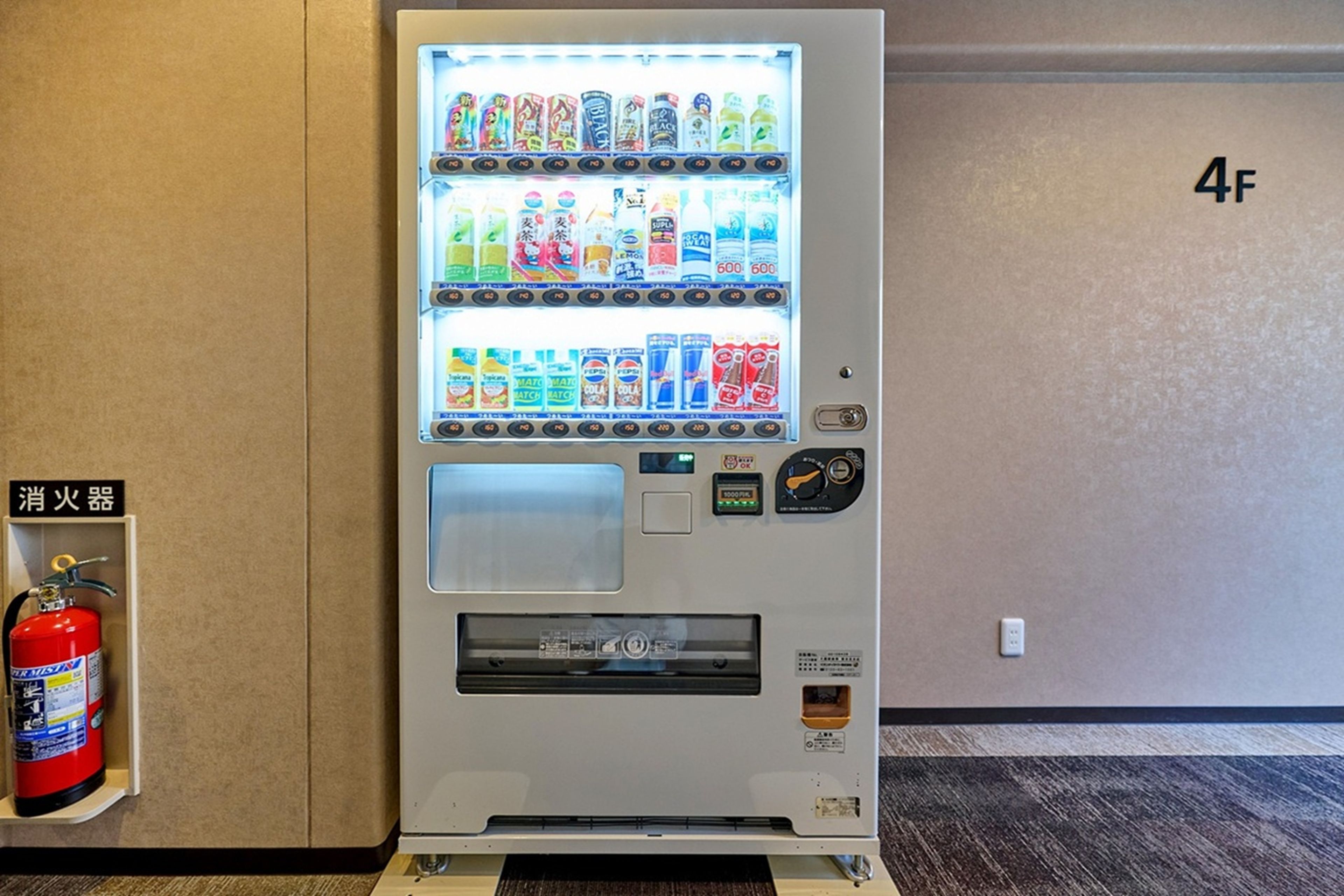 Máquina expendedora con diferentes bebidas y aperitivos, un extintor y el número de pared '4F'.