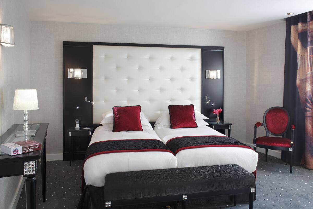 A hotel room with a large bed, two bedside tables, a chair, and a desk with a lamp.