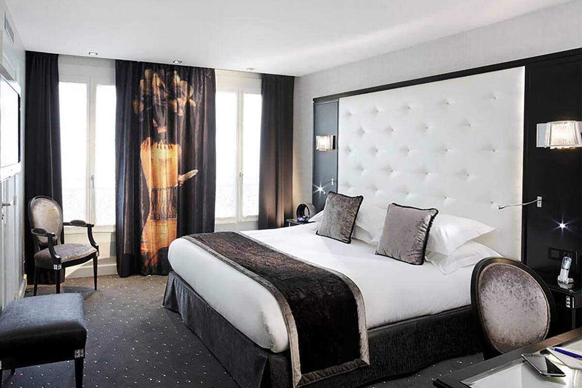 A hotel room with a large bed, a desk, a chair, and a view of the outdoors through the window.