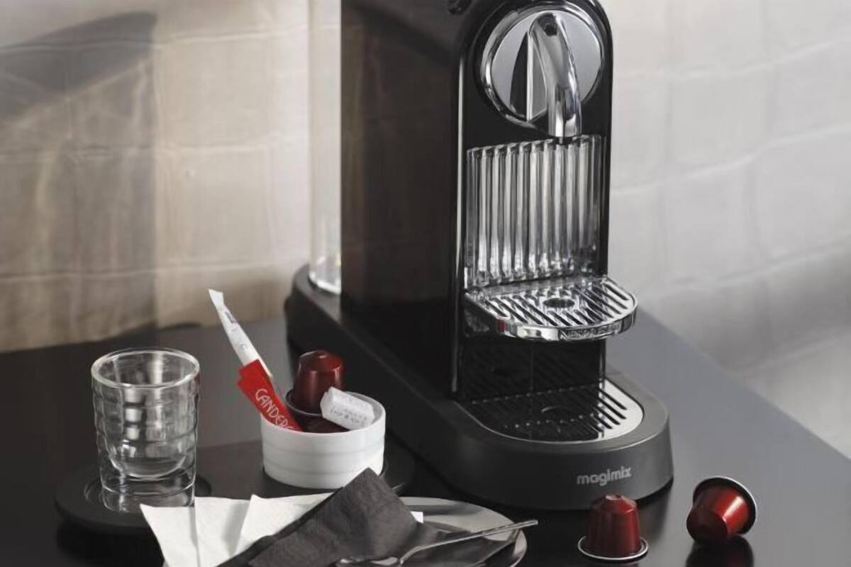 A coffee machine with a cup of coffee, a glass of water, and a napkin on a table.