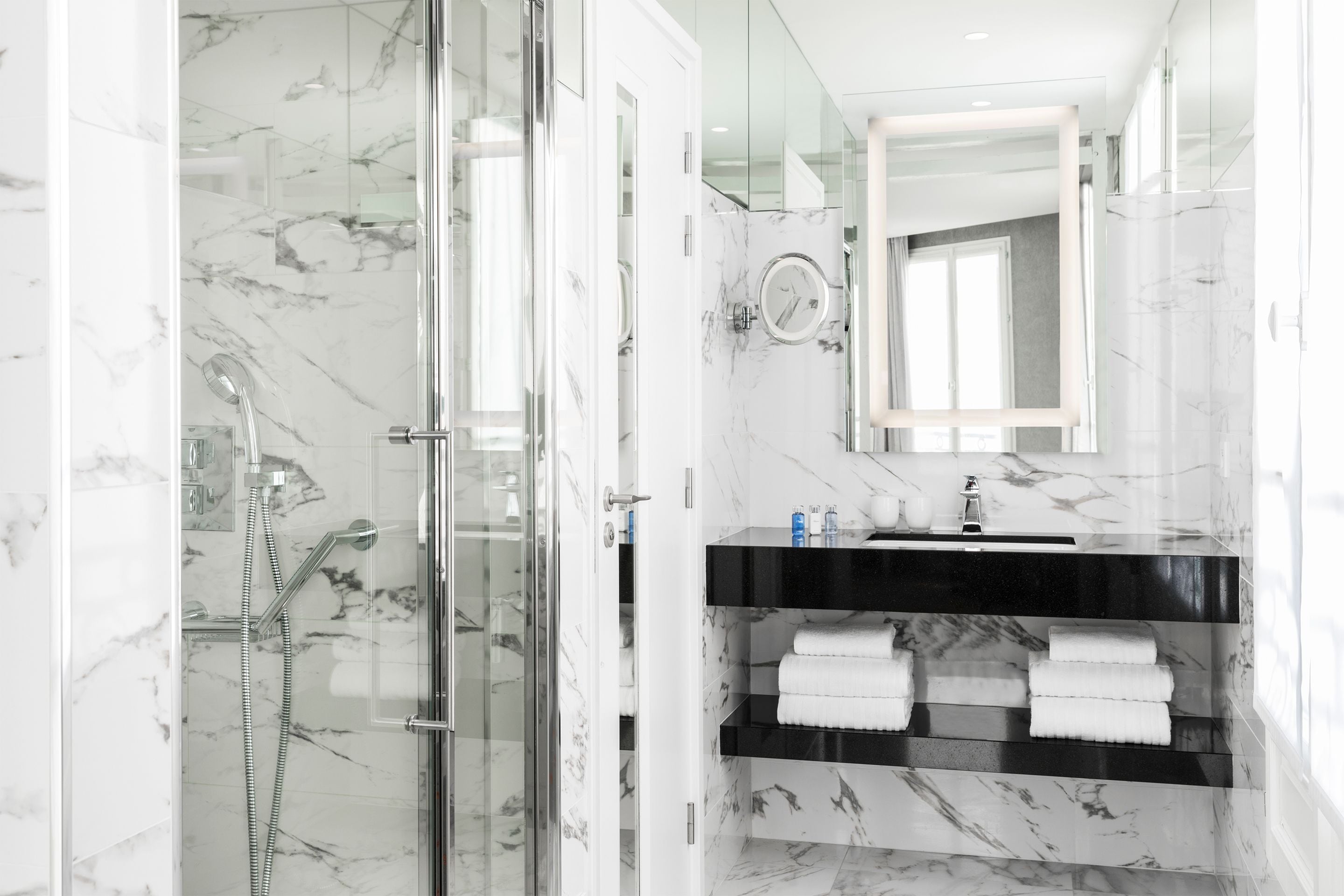 A modern bathroom with a glass-enclosed shower, a black sink vanity, and marble walls.