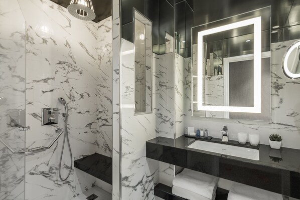 Un baño moderno con ducha envuelta en vidrio, un espejo grande y un mostrador negro con lavamanos.