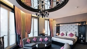 A hotel room with a curved ceiling, a large bed with a tufted headboard, a sofa with cushions, a round table, and a large mirror. - Maison Albar - Le Diamond (Paris)