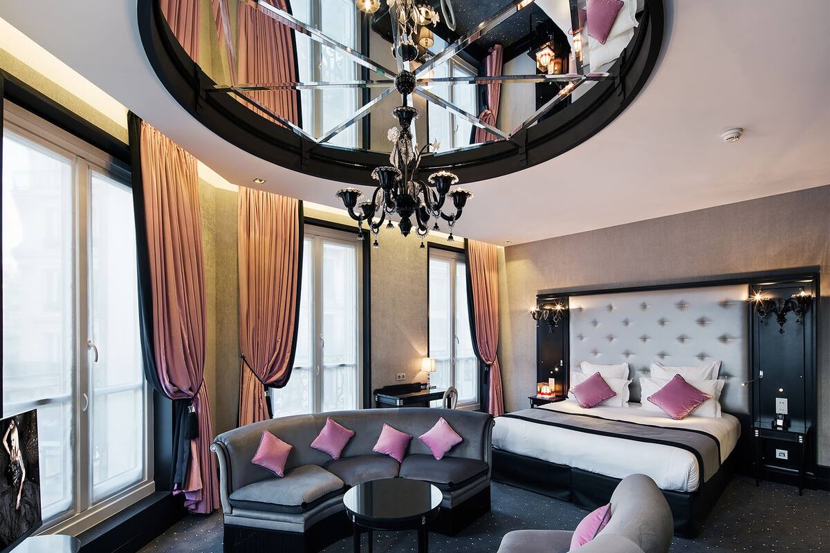 A hotel room with a curved ceiling, a large bed with a tufted headboard, a sofa with cushions, a round table, and a large mirror.