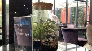 Een glazen terrarium met planten op een reflecterend zwart oppervlak, mogelijk in een hotellobby of openbare ruimte.