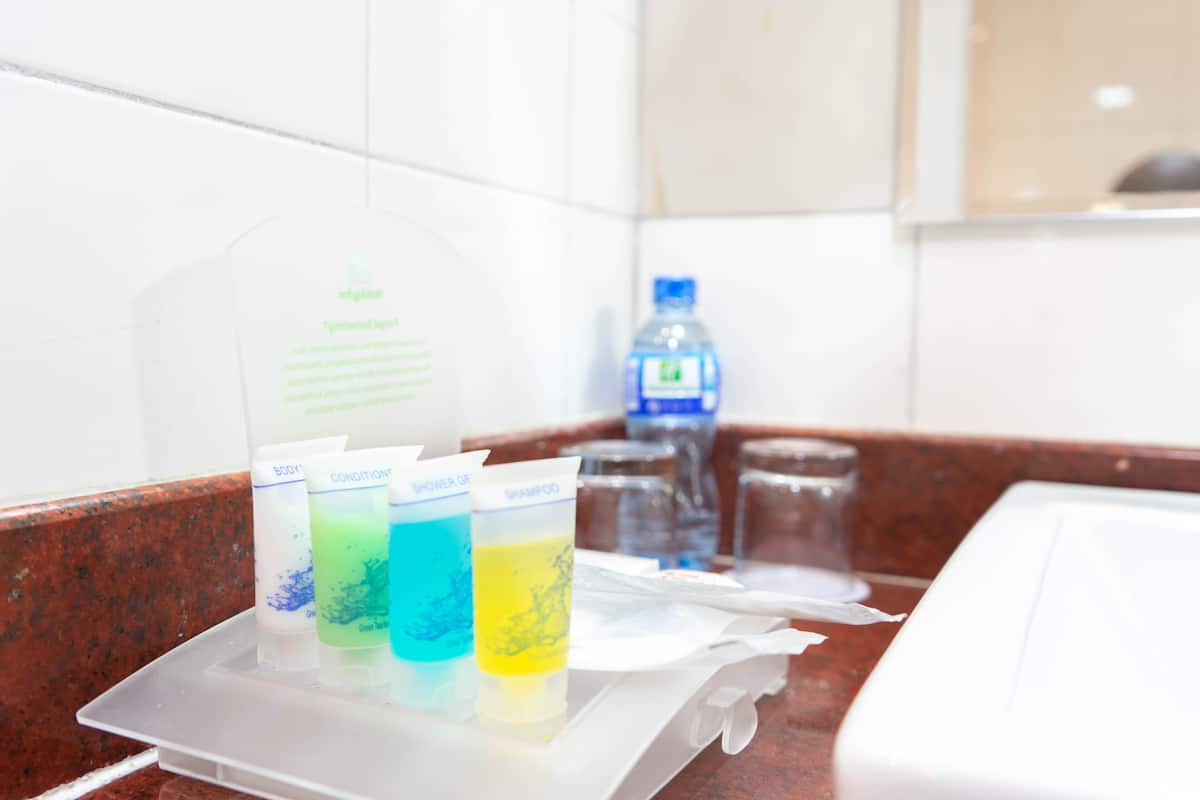 A bathroom counter with three bottles of shampoo and conditioner, a water bottle, and a tissue box.