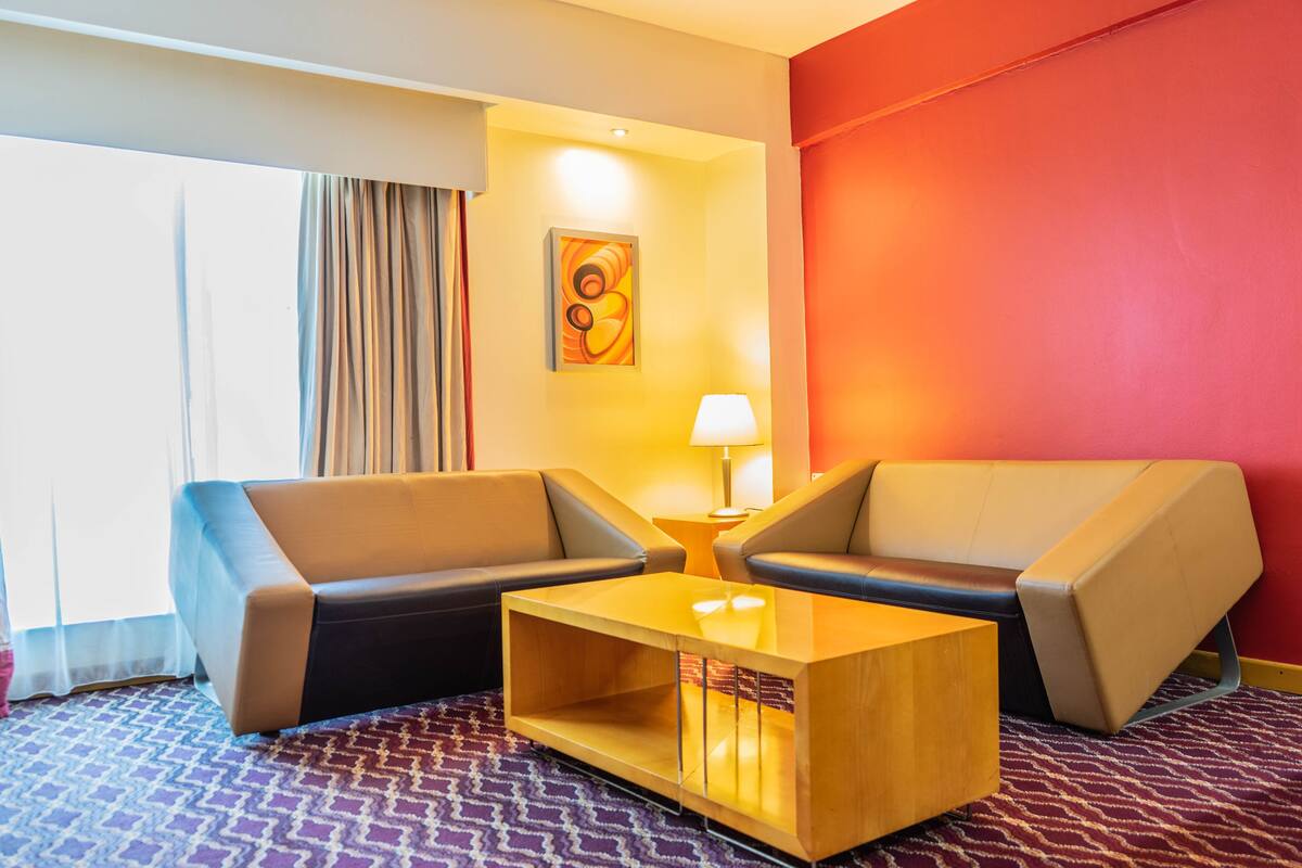 A hotel room with two sofas, a wooden coffee table, a lamp, and a painting on the wall.