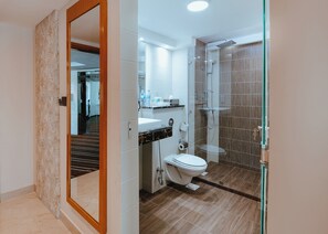 A modern bathroom with a toilet, sink, shower, and a glass door leading to a hallway.