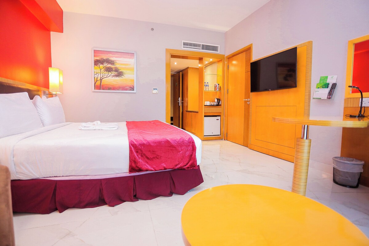Habitación de hotel con cama, televisión, escritorio y baño visible a través de una puerta abierta.