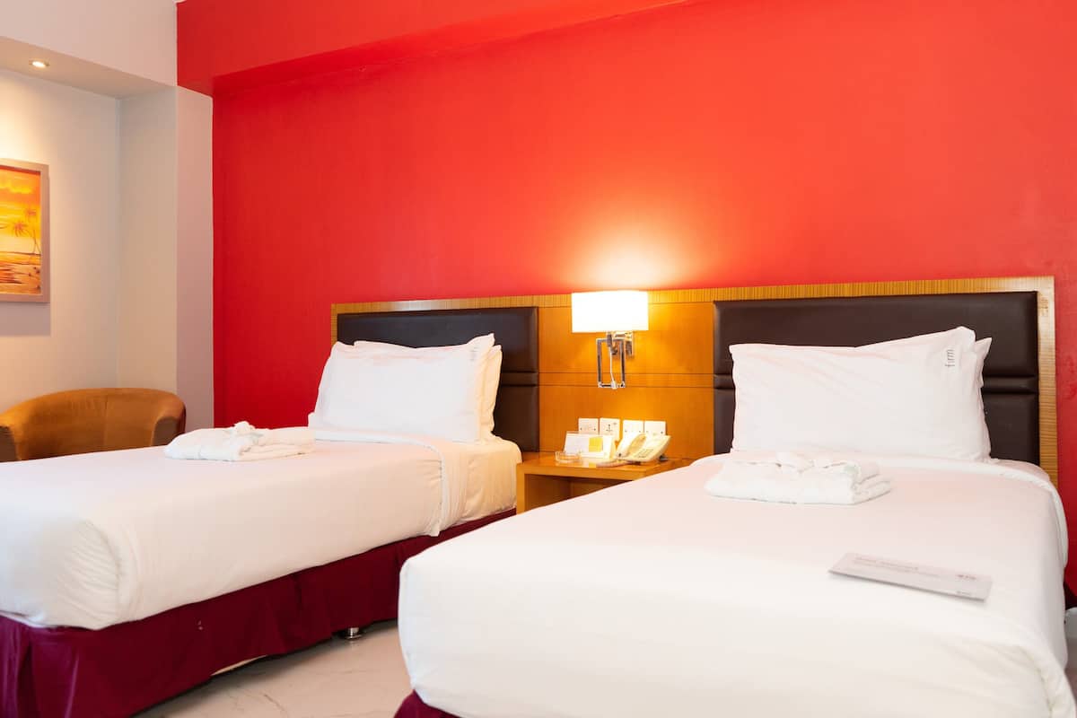 A hotel room with two beds, a nightstand with a phone, and a painting on the wall.