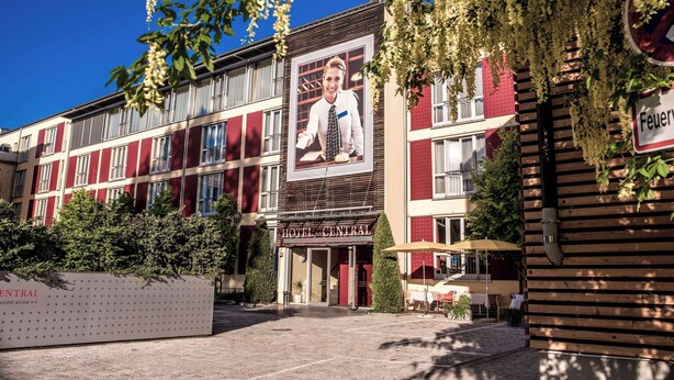 L’entrée d’un hôtel, avec une grande affiche, un panneau indiquant l’accès aux clients et un ciel dégagé.