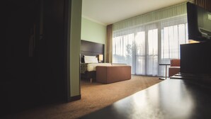 Une chambre d’hôtel avec un lit, un canapé, une télévision et une grande fenêtre avec des rideaux.