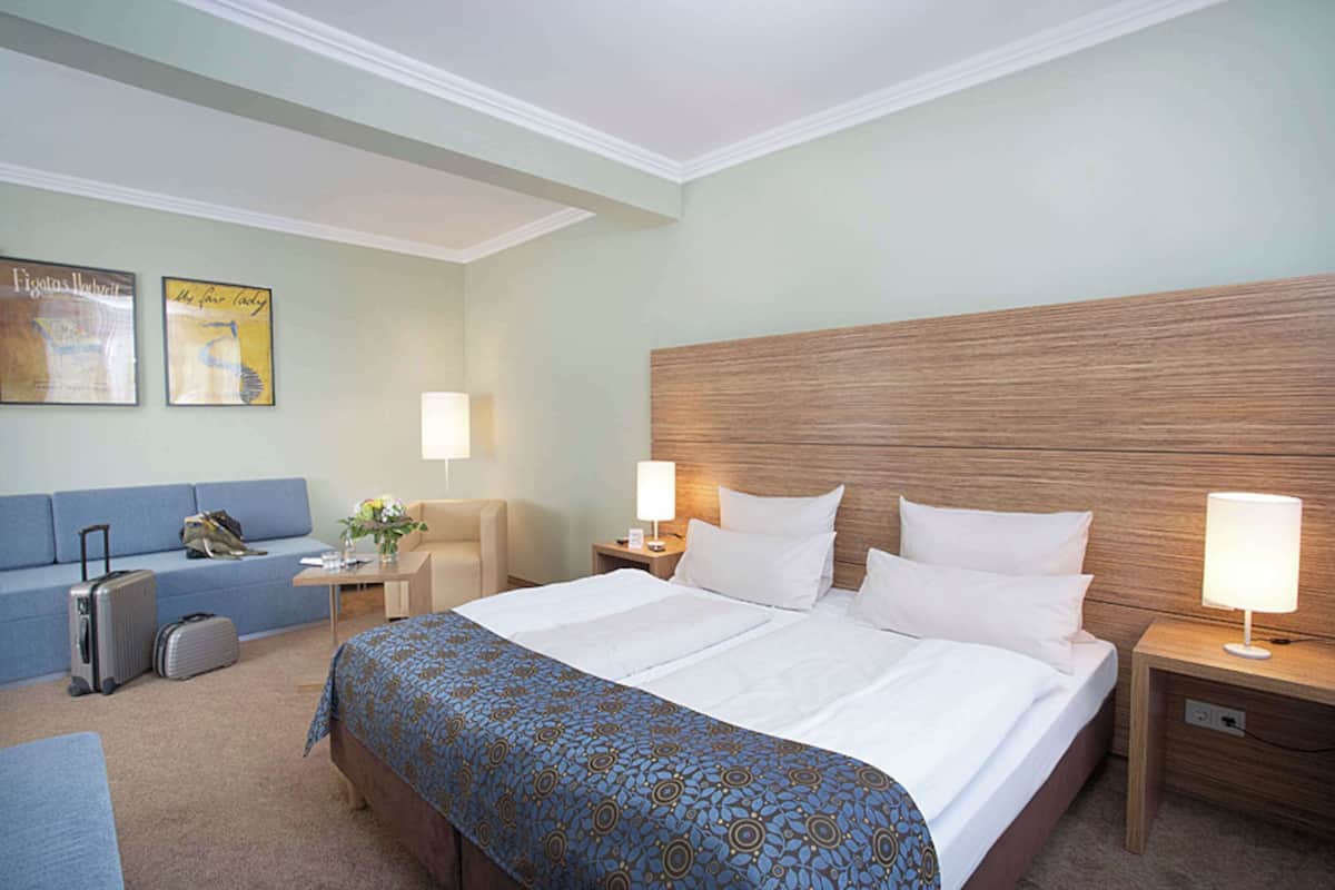 Une chambre d’hôtel avec un grand lit, un canapé, un bureau avec une lampe et une table de chevet avec une lampe.