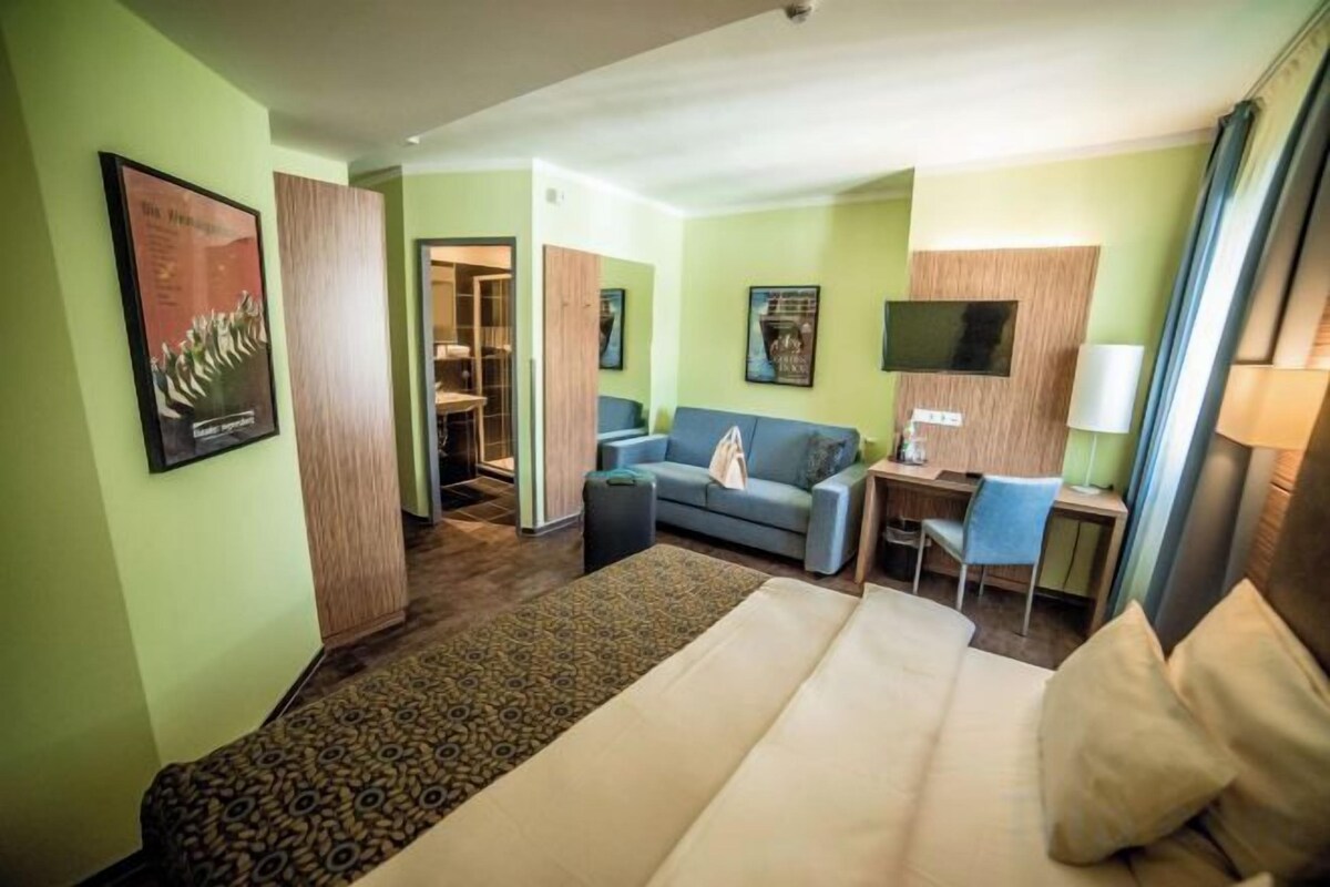 A hotel room with a bed, a desk, a chair, a sofa, and a television.