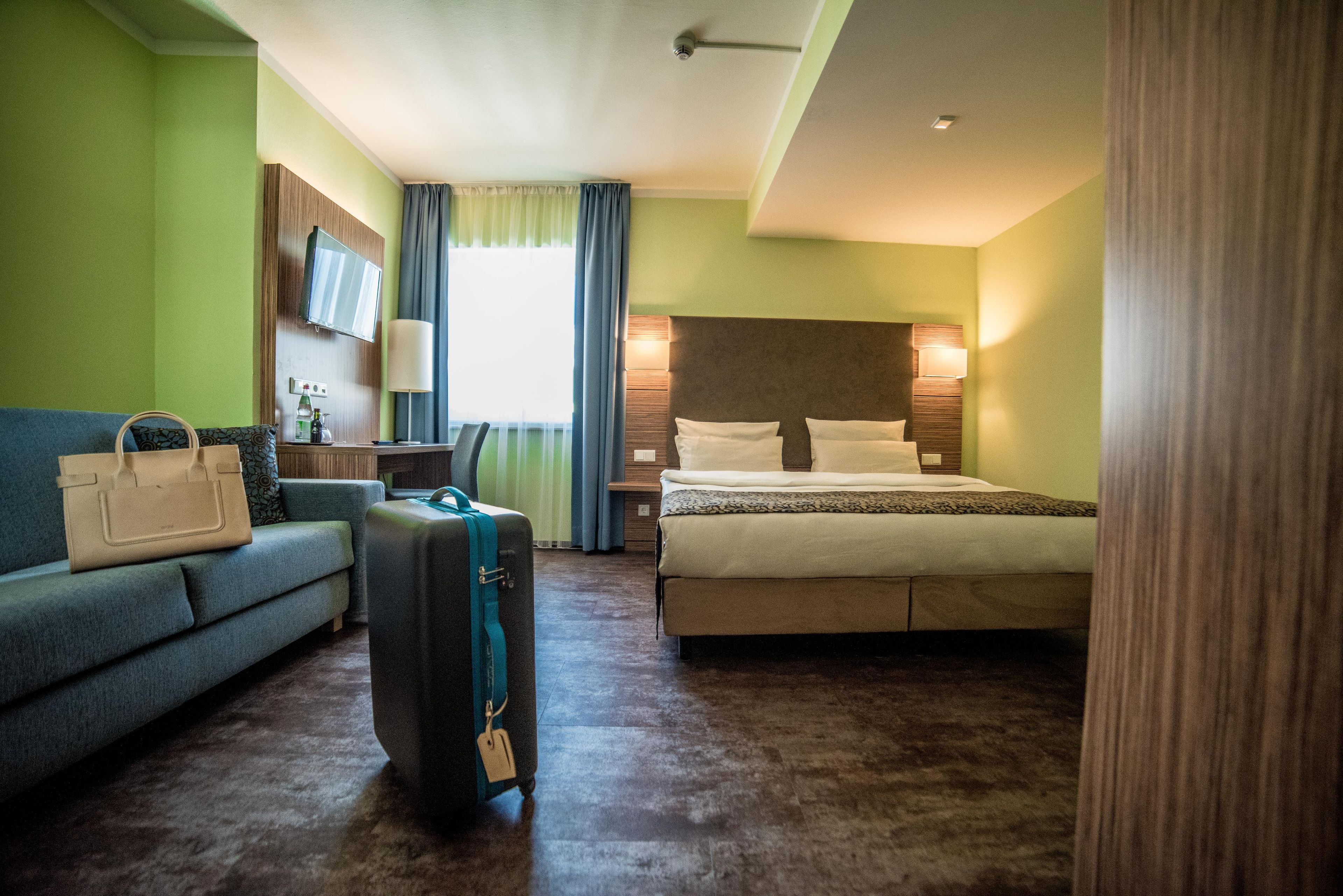 Una habitación de hotel con cama, sofá, escritorio, televisor y maleta.