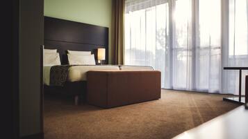 A hotel room with a bed, an ottoman, a nightstand, and a window with curtains.
