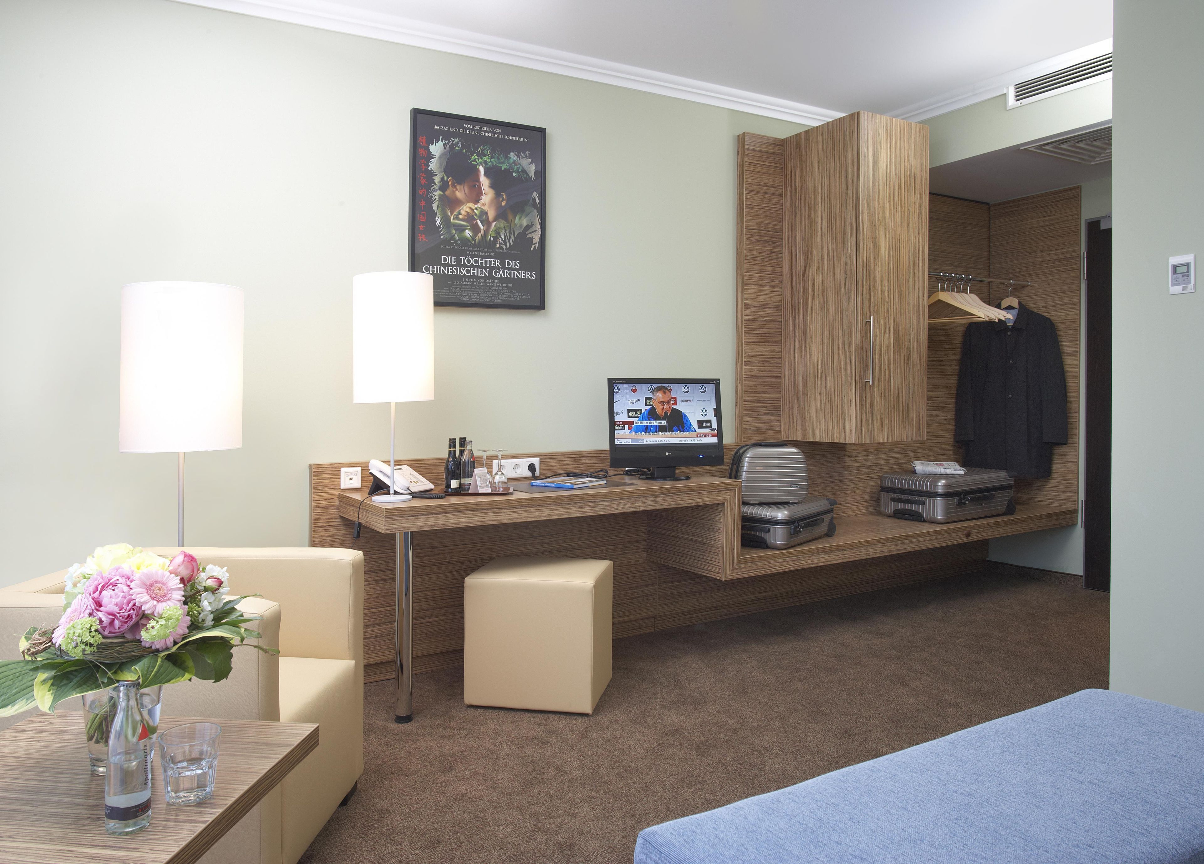 A hotel room with a desk, a computer, a TV, a wardrobe, and a bed.