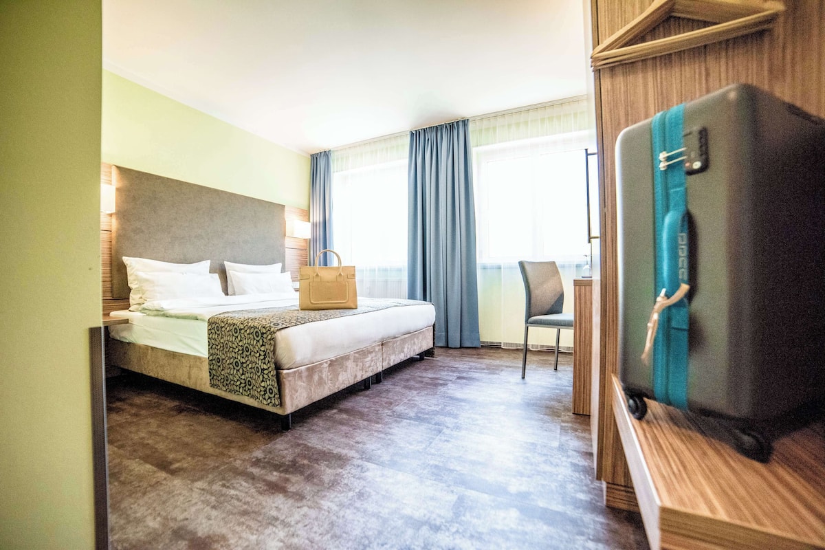 Une chambre d’hôtel avec un lit, une chaise, un bureau et une valise.