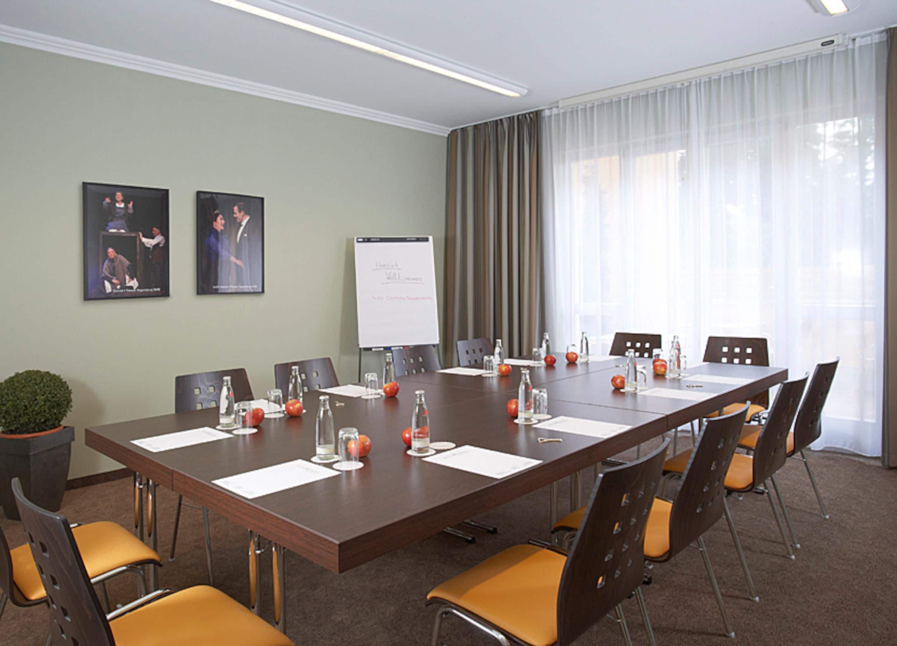 A conference room with a long table, chairs, a whiteboard, and framed pictures on the wall.
