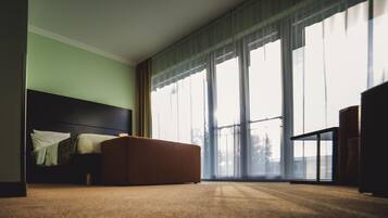 Habitación de hotel con una cama grande, un reposapiés marrón y vistas de la ciudad a través de amplias ventanas.