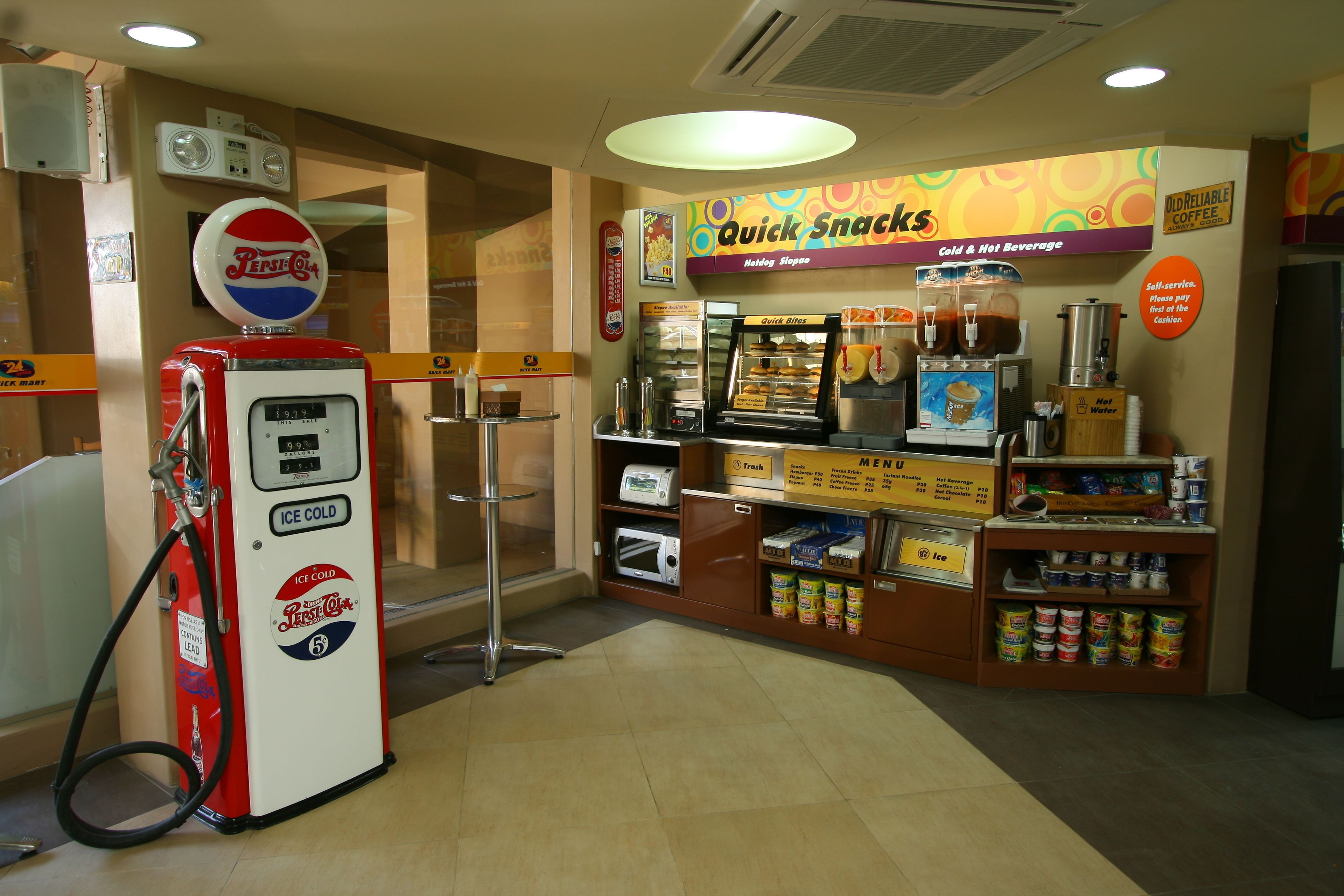 A fast-food restaurant with a Pepsi gas pump, a self-service coffee station, and a variety of food items on display.