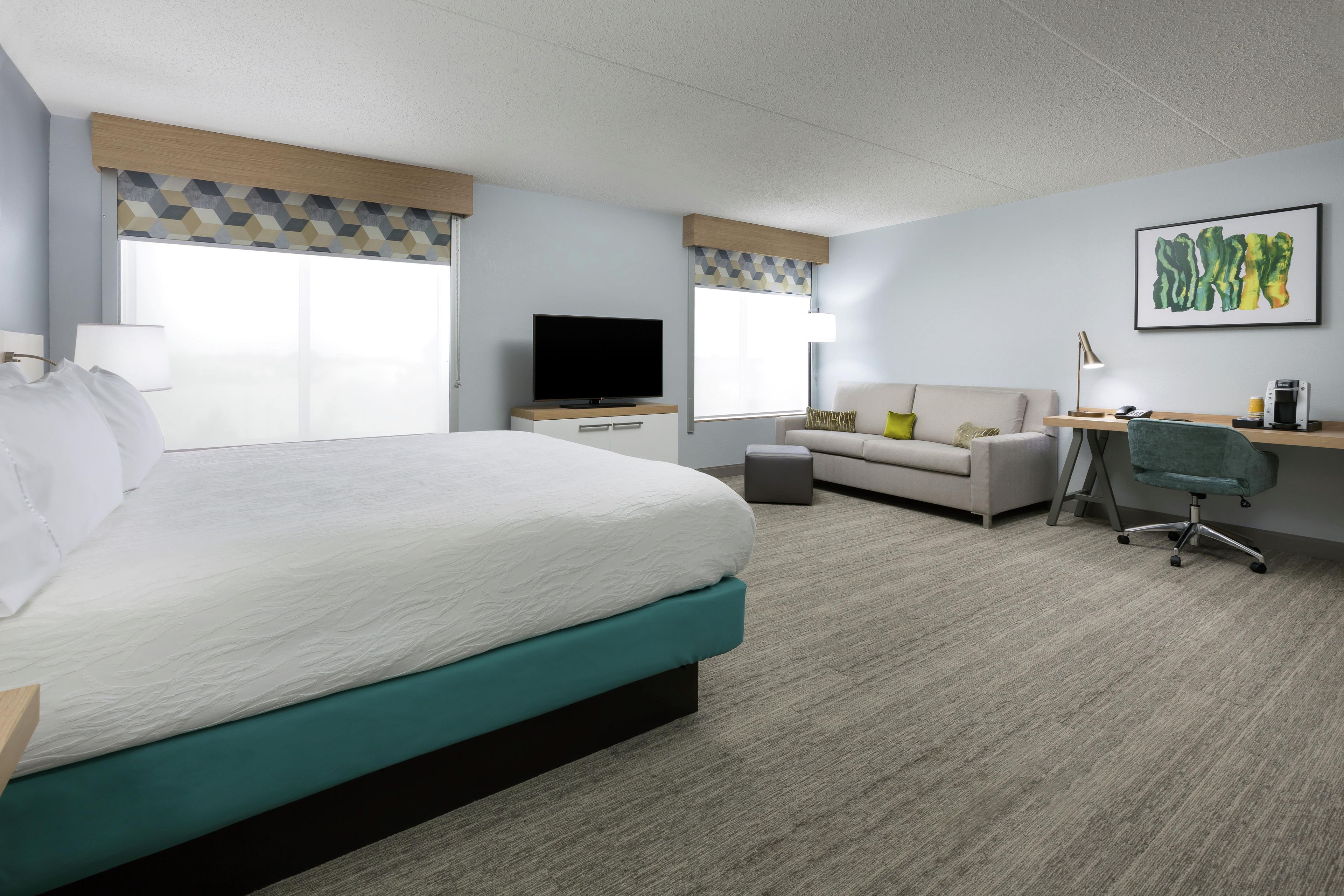 Habitación de hotel con una cama grande, un sofá, un escritorio con silla, un televisor y una cafetera.