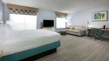 Habitación de hotel con una cama grande, un sofá, un escritorio con silla, un televisor y una cafetera.