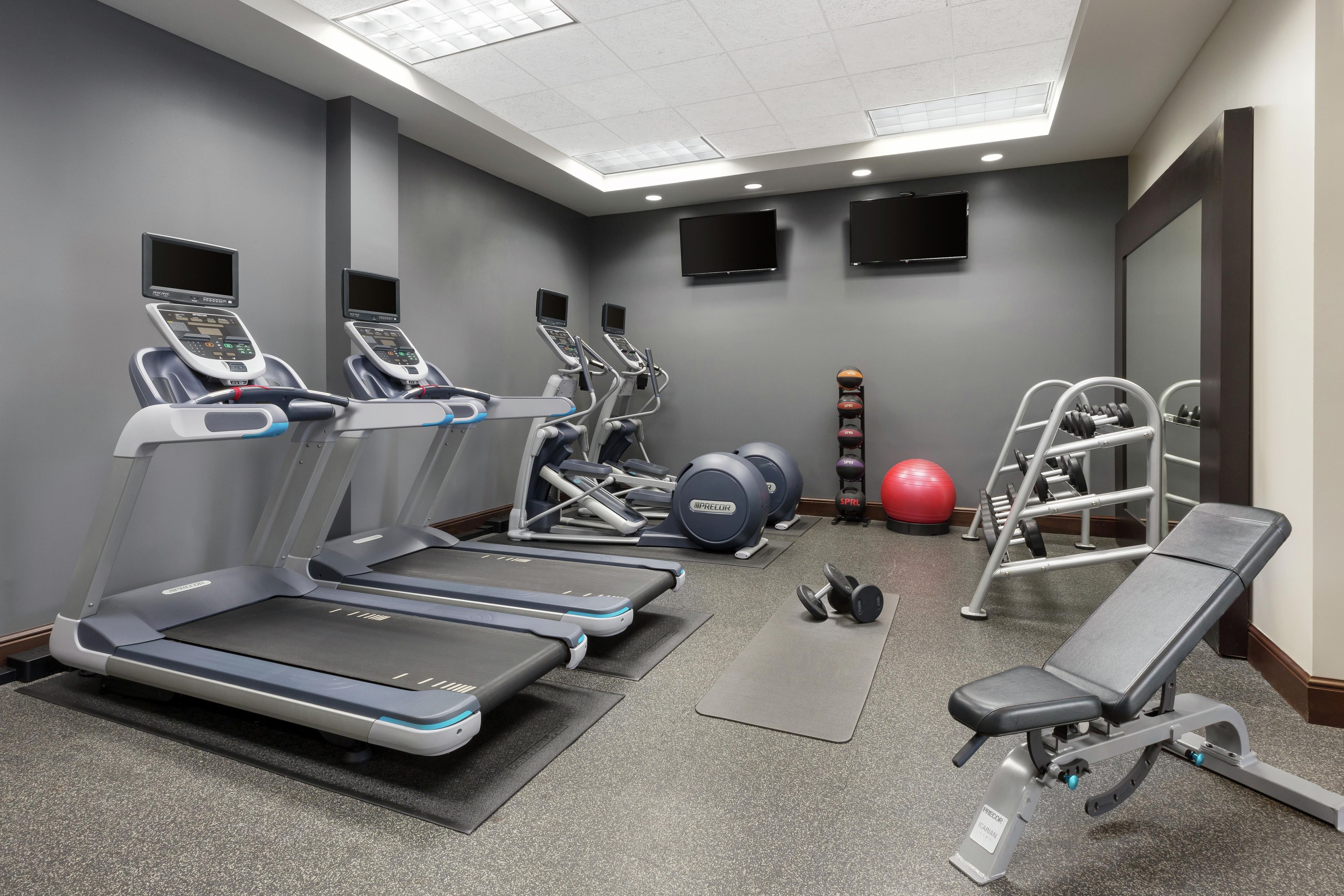 Une salle de sport équipée de tapis de course, d’appareils de musculation, d’un banc et de ballons d’exercice.