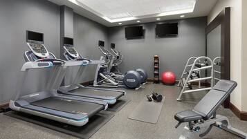 Une salle de sport équipée de tapis de course, d’appareils de musculation, d’un banc et de ballons d’exercice.